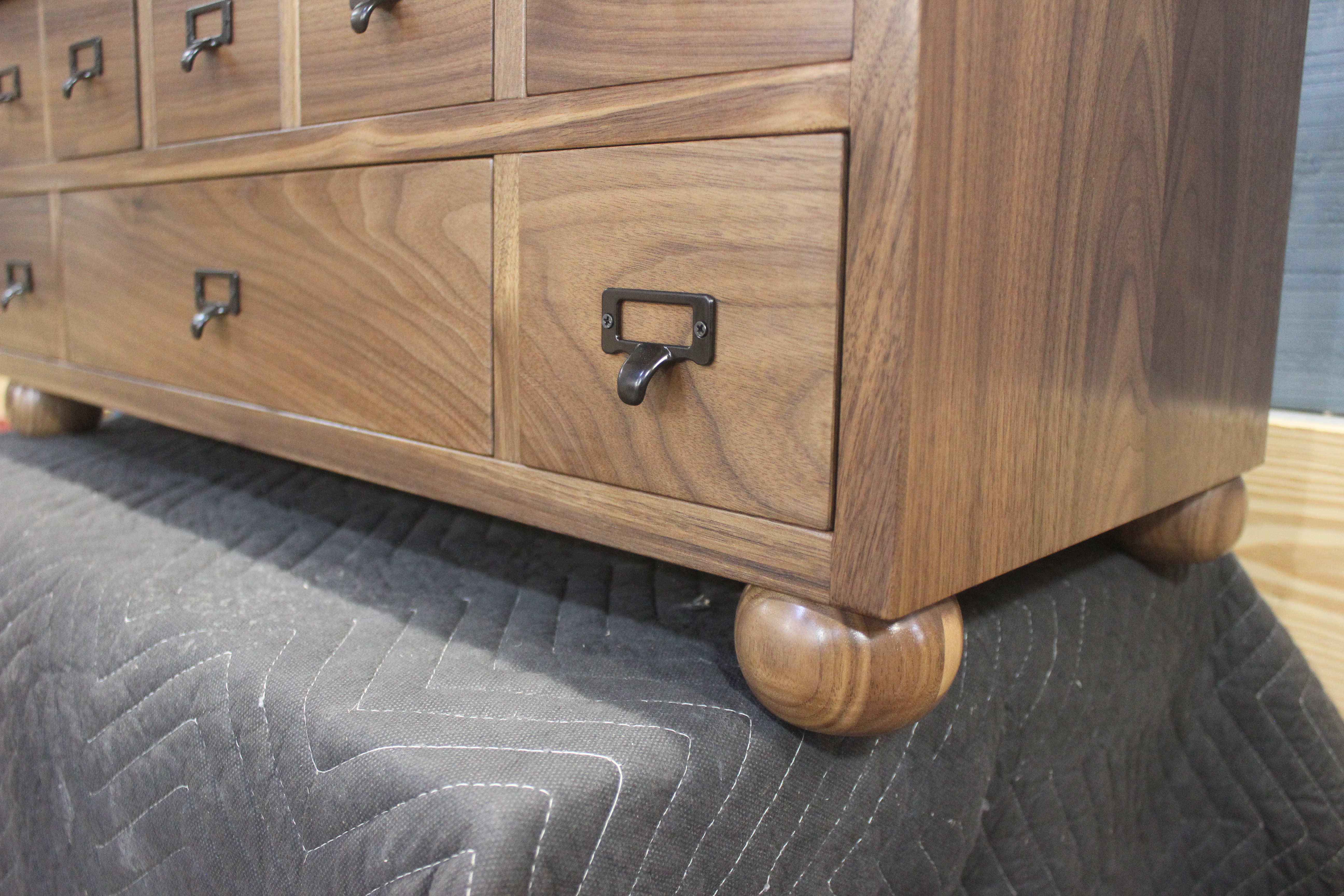 Close-up view of a wooden cabinet with multiple drawers and black metal handles, resting on a padded surface.