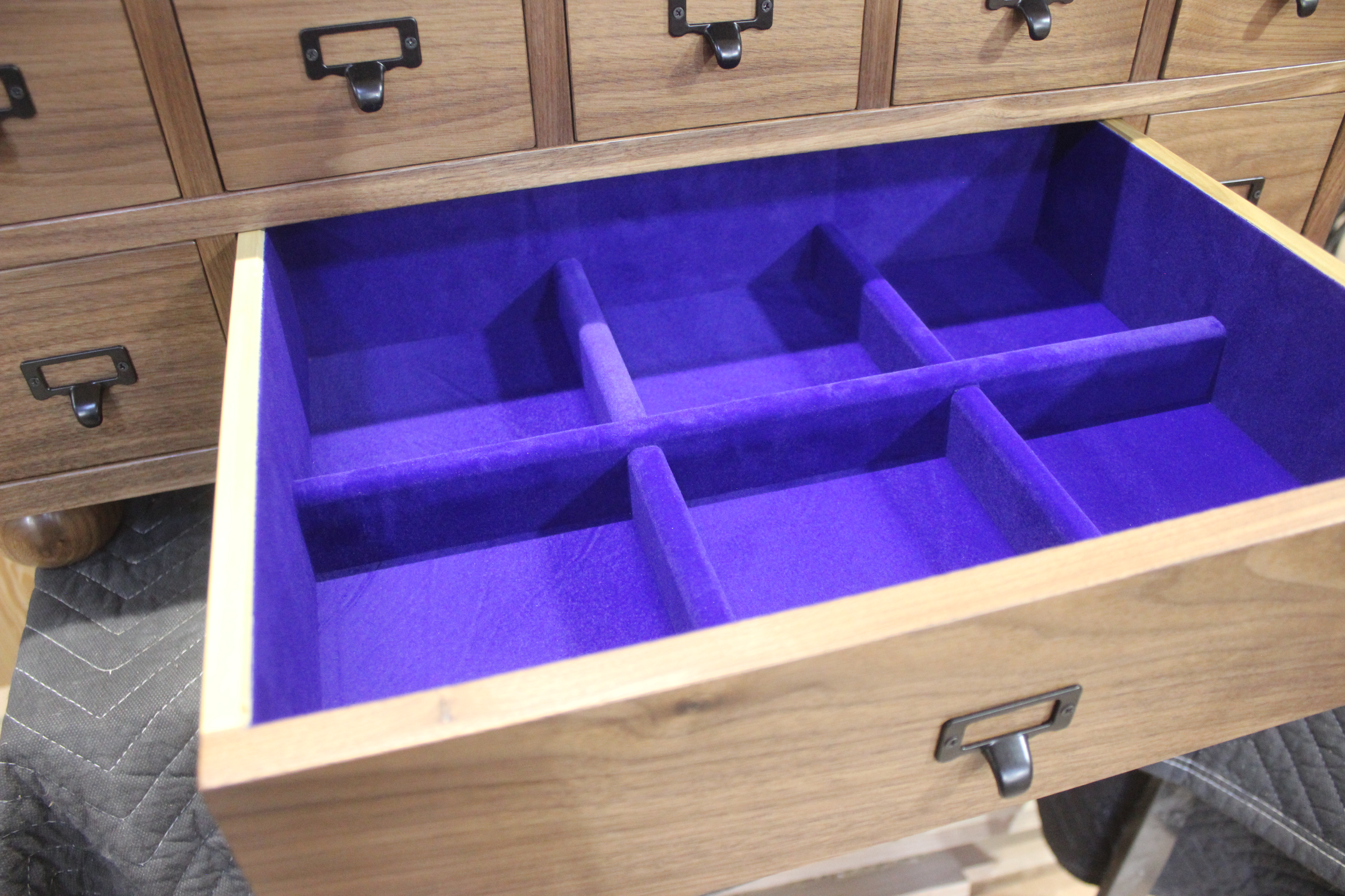 An open wooden drawer with a vibrant purple felt lining, featuring multiple compartments.