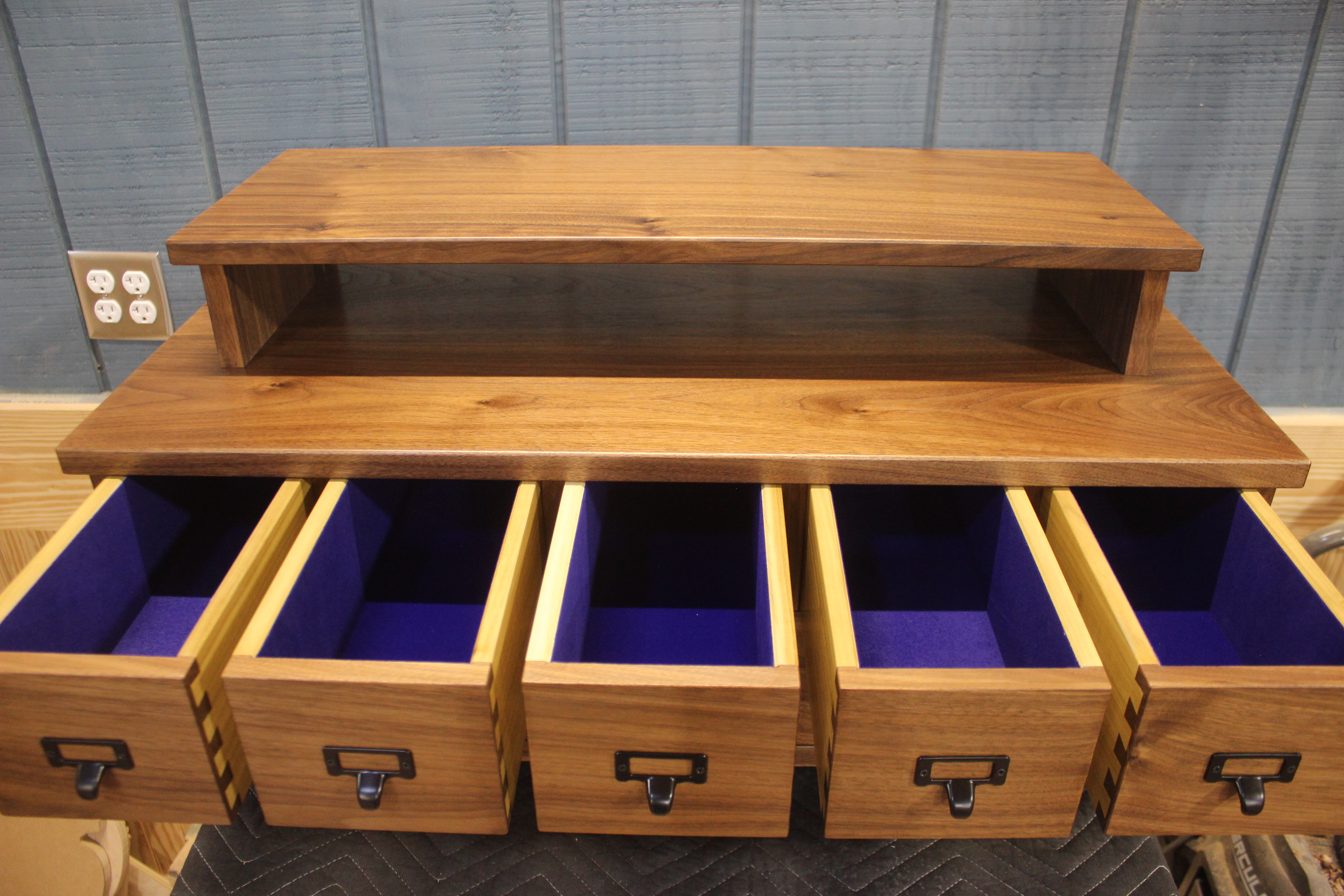 A wooden storage unit with a flat top shelf and five open drawers, featuring a purple interior.