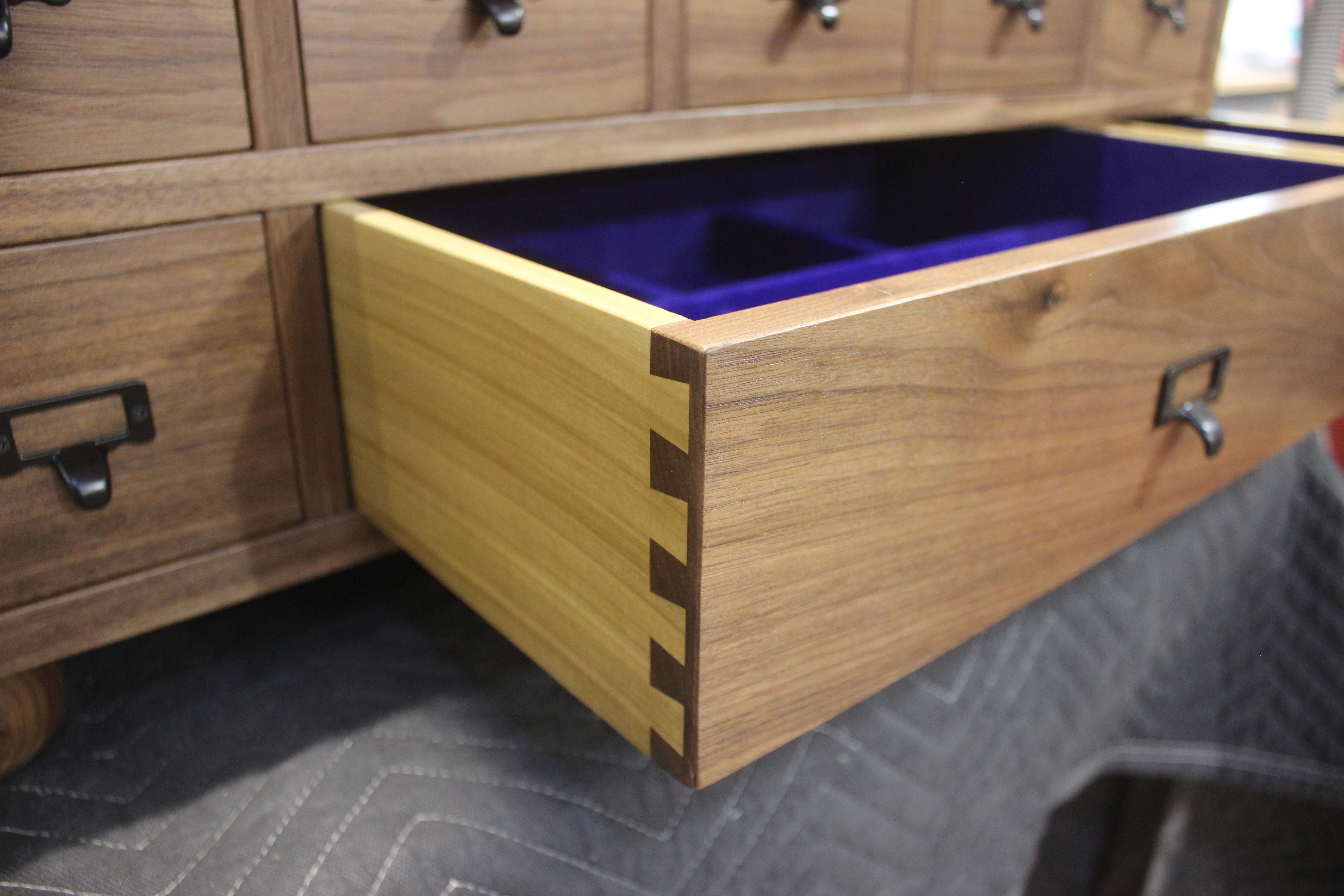Close-up of a wooden drawer partially opened, showcasing a contrasting light and dark wood joinery with a purple interior.