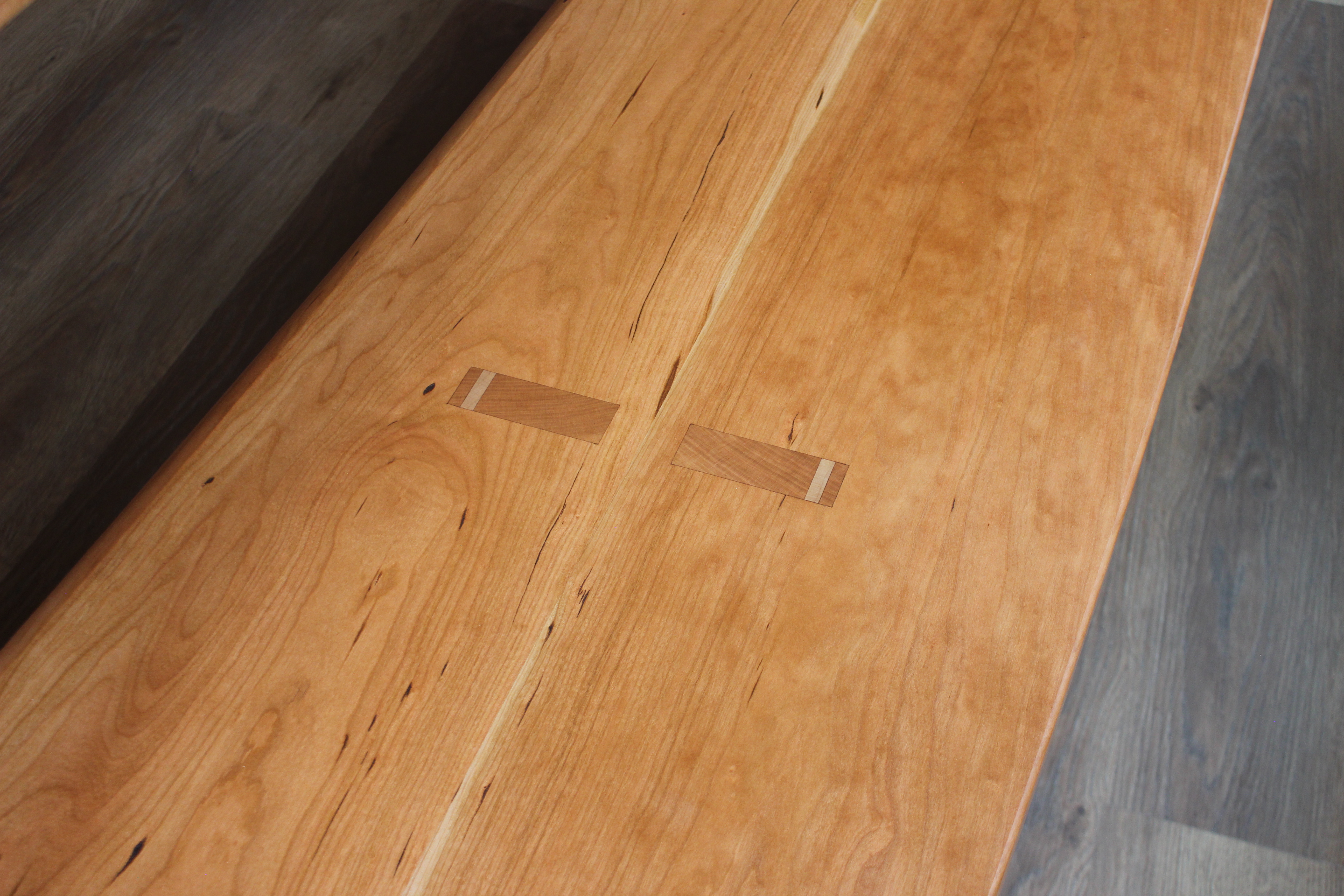 Close-up view of a wooden tabletop with contrasting inlay joints in a smooth, polished finish.