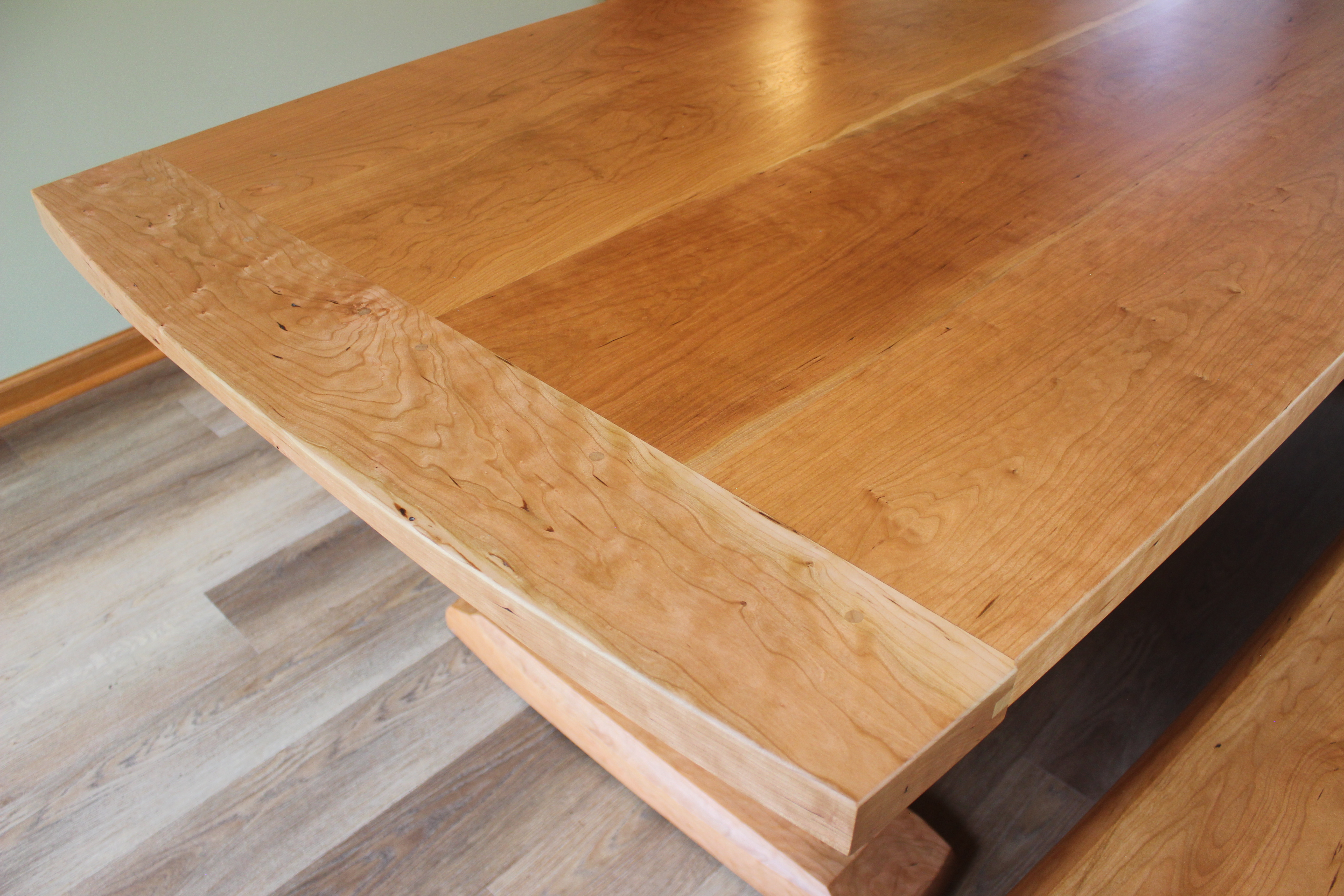 Close-up view of a wooden dining table showcasing a smoothly finished cherry wood surface with grain patterns and a rounded edge.