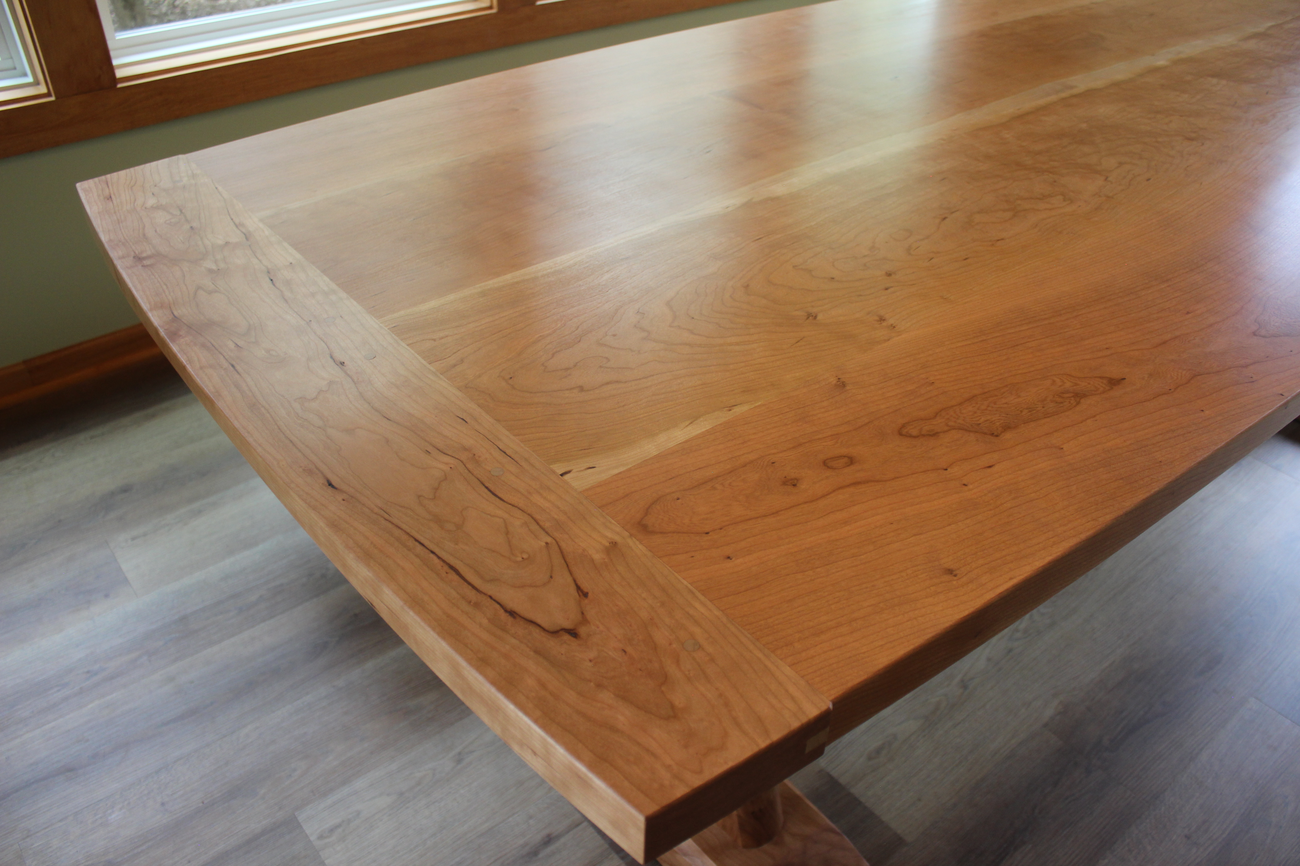 Close-up of a polished wooden table with a smooth, curved edge and a glossy finish, highlighting the natural grains of the wood.
